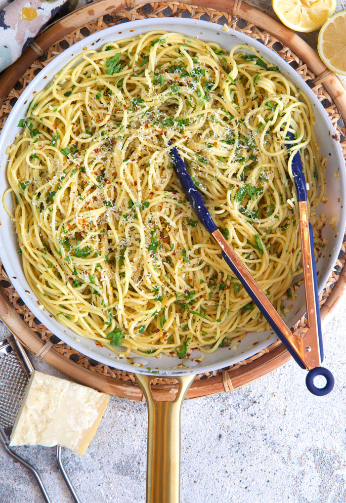 pasta aglio e olio in a skillet with tongs after being cooked.