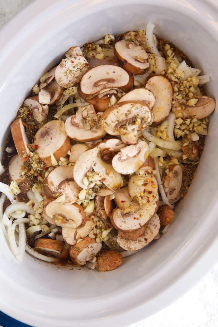 ingredients for slow cooker chicken cheesesteak layered in a crock pot