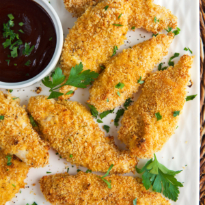 Baked Chicken Tenders on a white platter with a bowl of bbq sauce.
