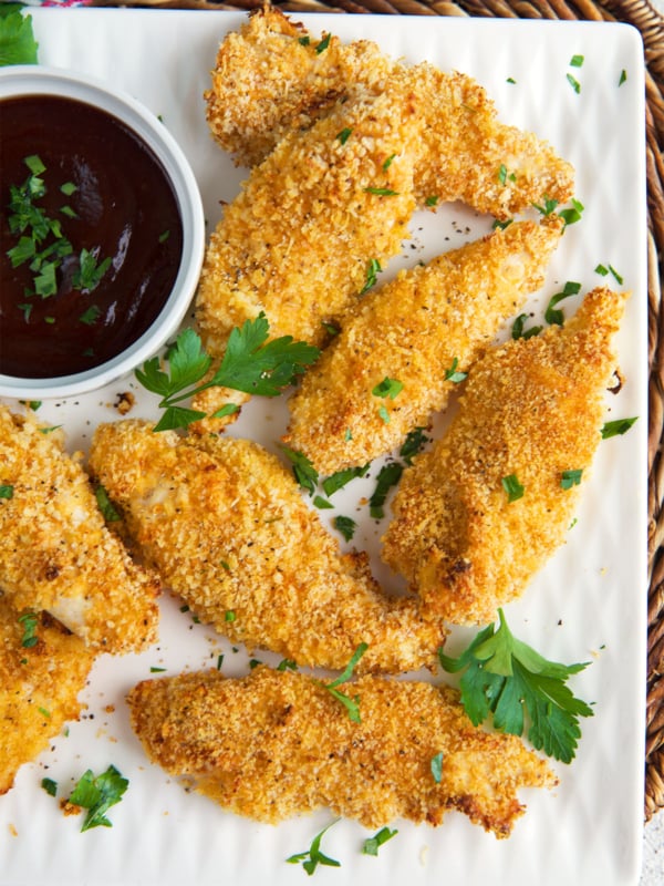 Baked Chicken Tenders on a white platter with a bowl of bbq sauce.