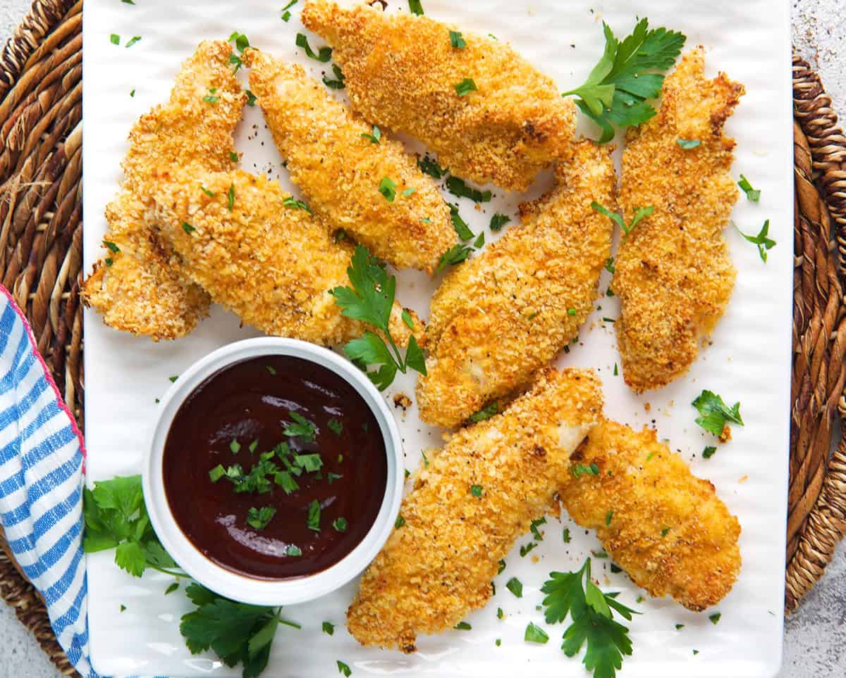 chicken tenders on a white platter with a bowl of sauce