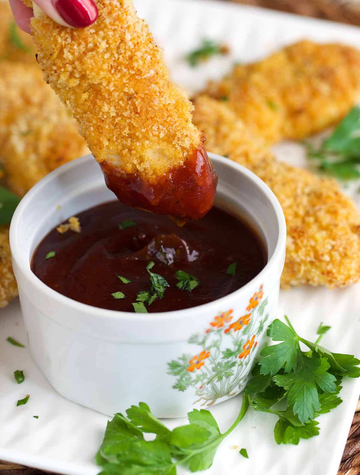 Chicken tender being dipped in BBQ sauce.