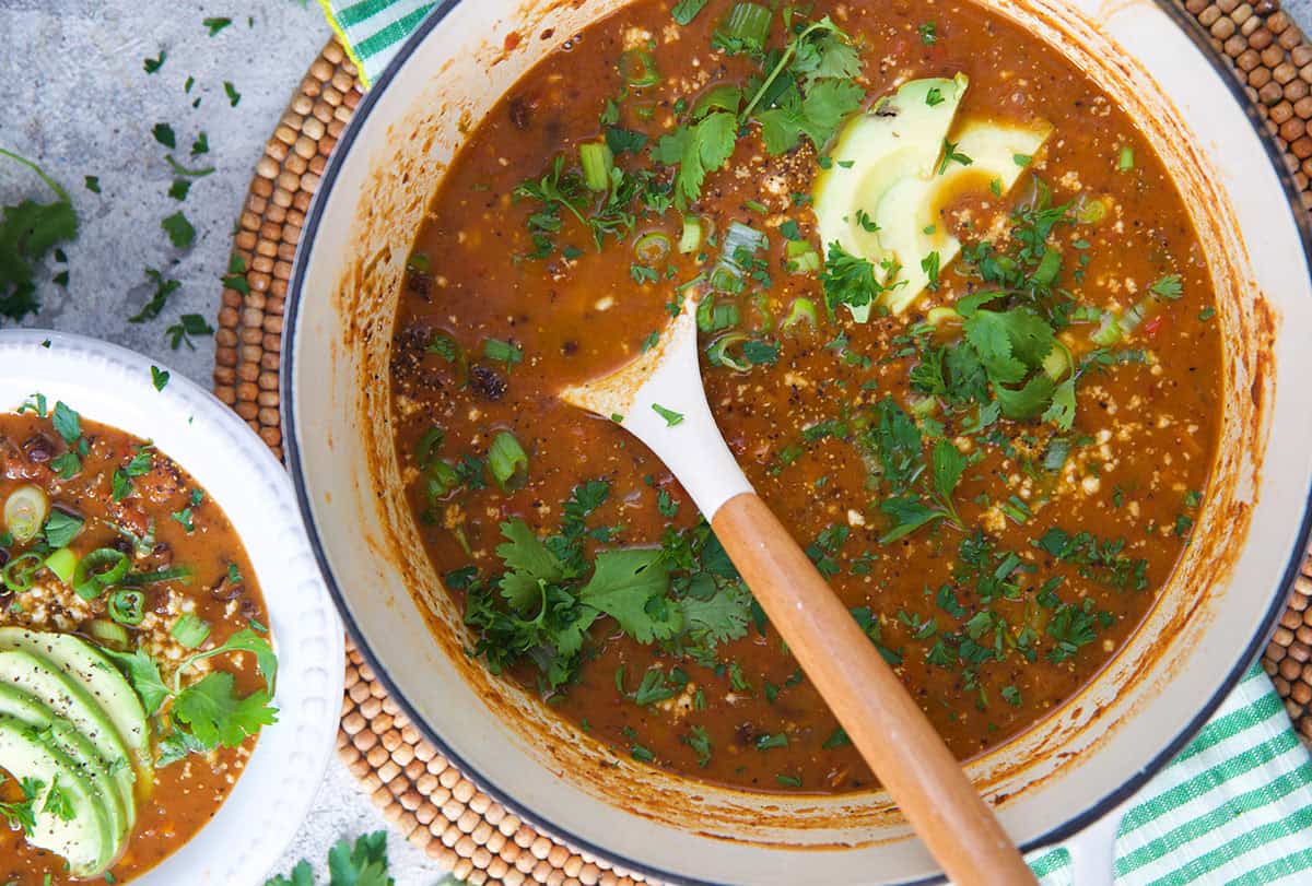 Black bean soup in a dutch oven with a white and wooden ladle.
