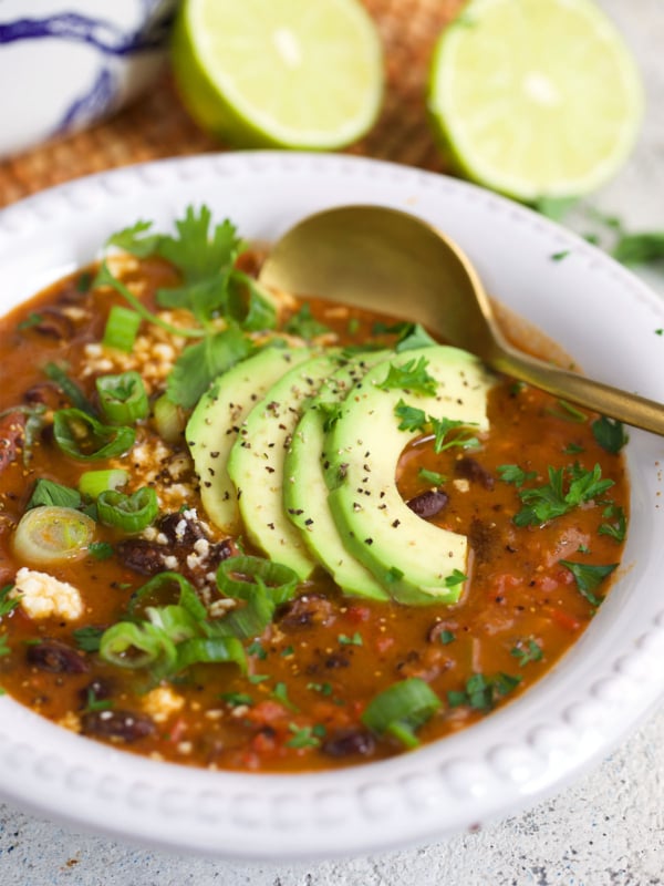 Black Bean Soup in a white bowl with sliced avocado on top and a gold spoon