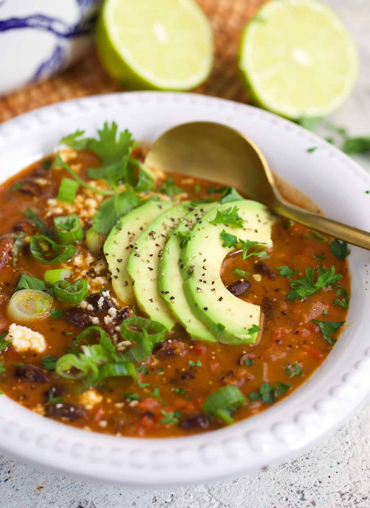 Black Bean Soup in a white bowl with sliced avocado on top and a gold spoon