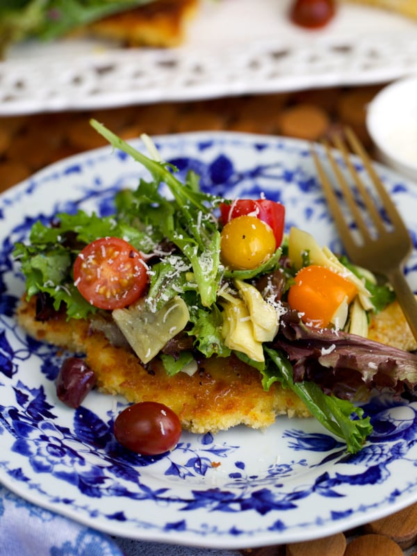 chicken milanese on a blue and white plate topped with a light salad.