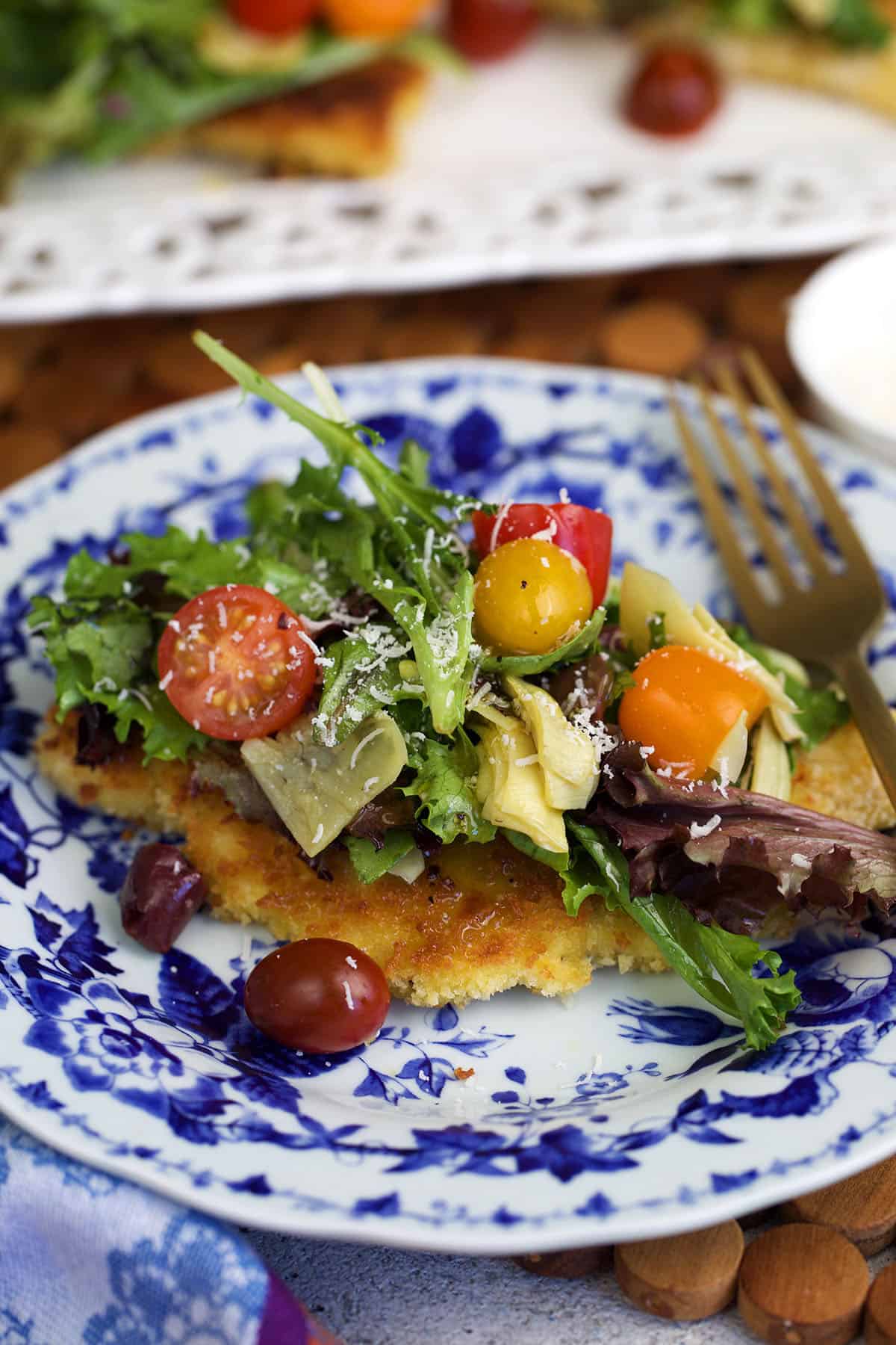 chicken milanese on a blue and white plate topped with a light salad.