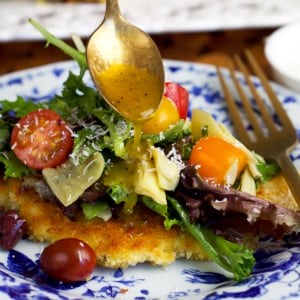 Crispy chicken milanese on a blue and white plate with dressing being drizzled over top.