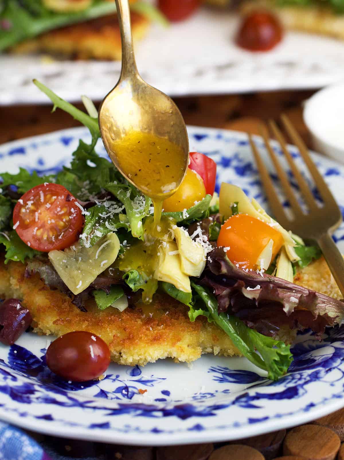 Crispy chicken milanese on a blue and white plate with dressing being drizzled over top.