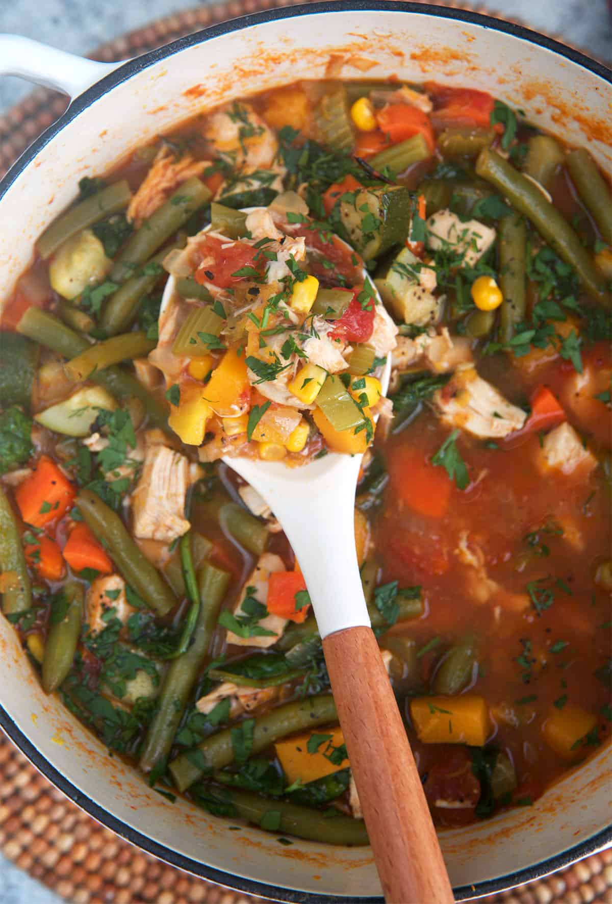 Chicken Vegetable Soup in a dutch oven with a white ladle scooping up a serving.