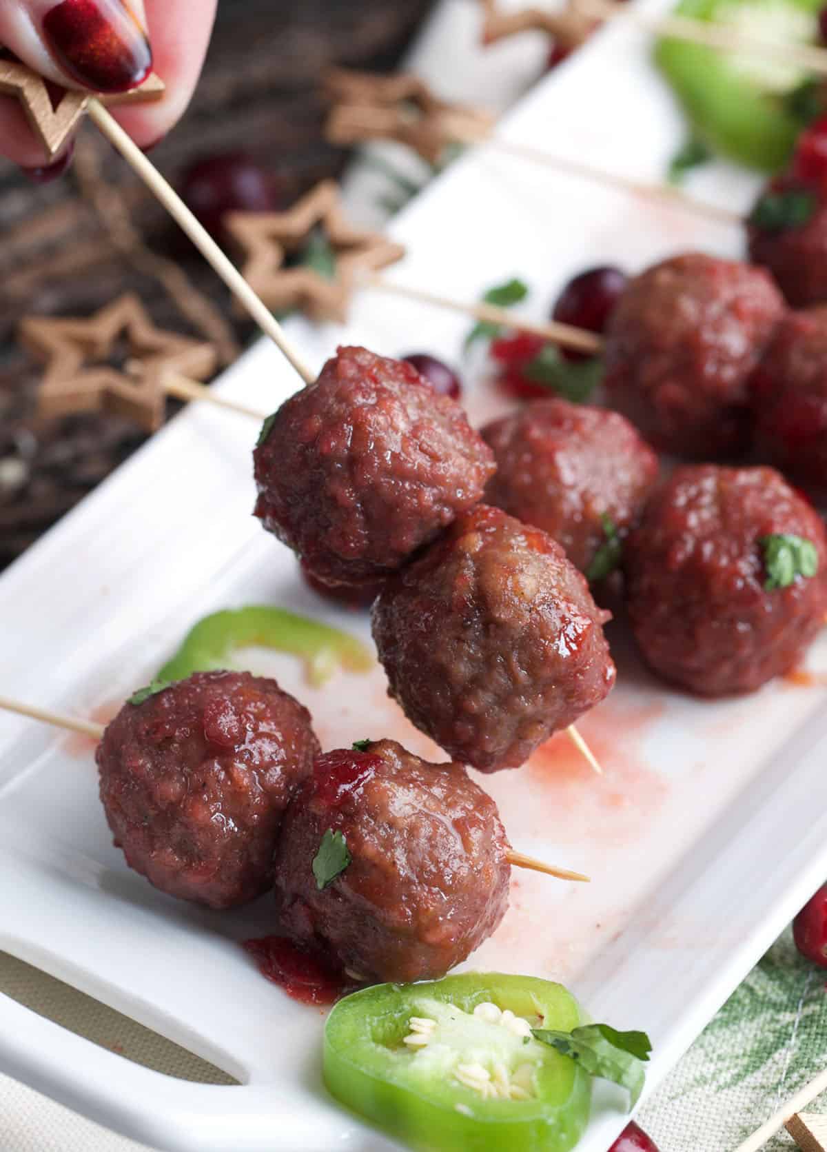 cranberry meatballs on a cocktail pick with more arranged on a platter