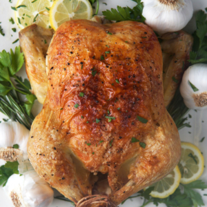 Engagement Chicken on a white platter with lemons, herbs and garlic.