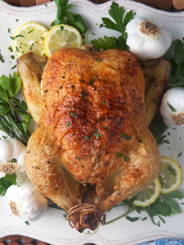 Engagement Chicken on a white platter with lemons, herbs and garlic.