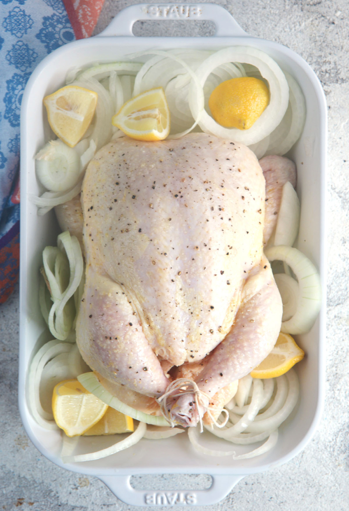 whole chicken with onions and lemons in a roasting pan