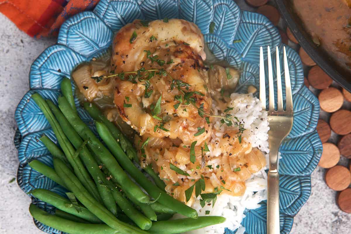 French onion pork chop on a blue plate with green beans and mashed potatoes