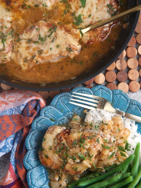 French onion pork chops in a skillet with one chop on a blue plate with green beans