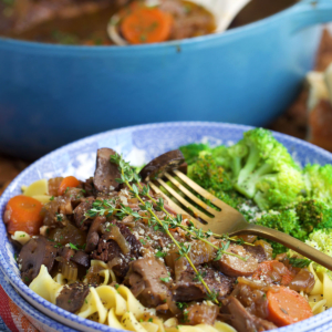 French onion pot roast on egg noodles in a bowl with broccoli on the side.