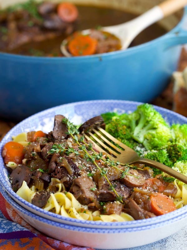 French onion pot roast on egg noodles in a bowl with broccoli on the side.