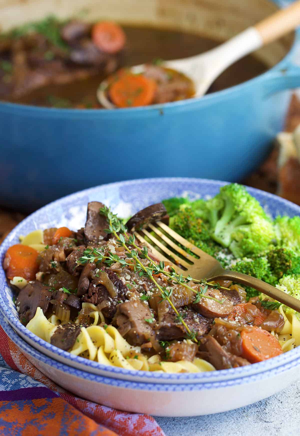 French onion pot roast on egg noodles in a bowl with broccoli on the side.