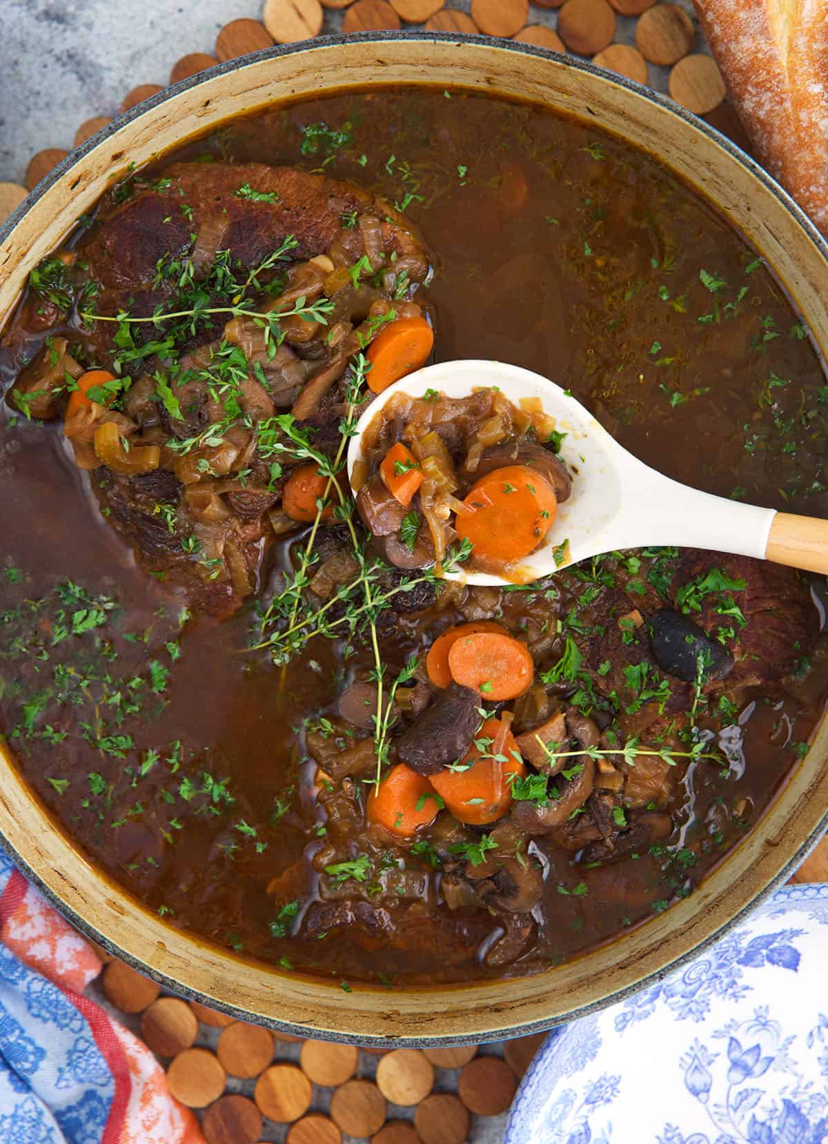 French Onion Pot Roast in a round dutch oven with a white and wood serving ladle.