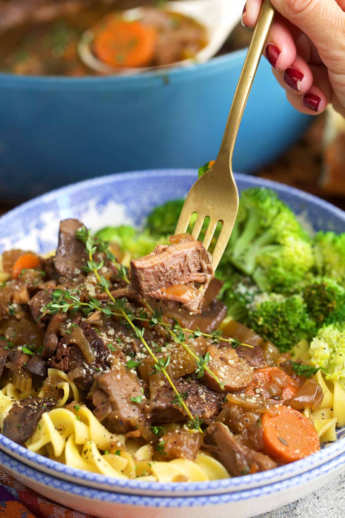 French Onion Pot roast served over egg noodles with a gold fork ready for a bite.