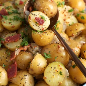 German Potato Salad in a serving bowl with a serving spoon ready to serve a portion.
