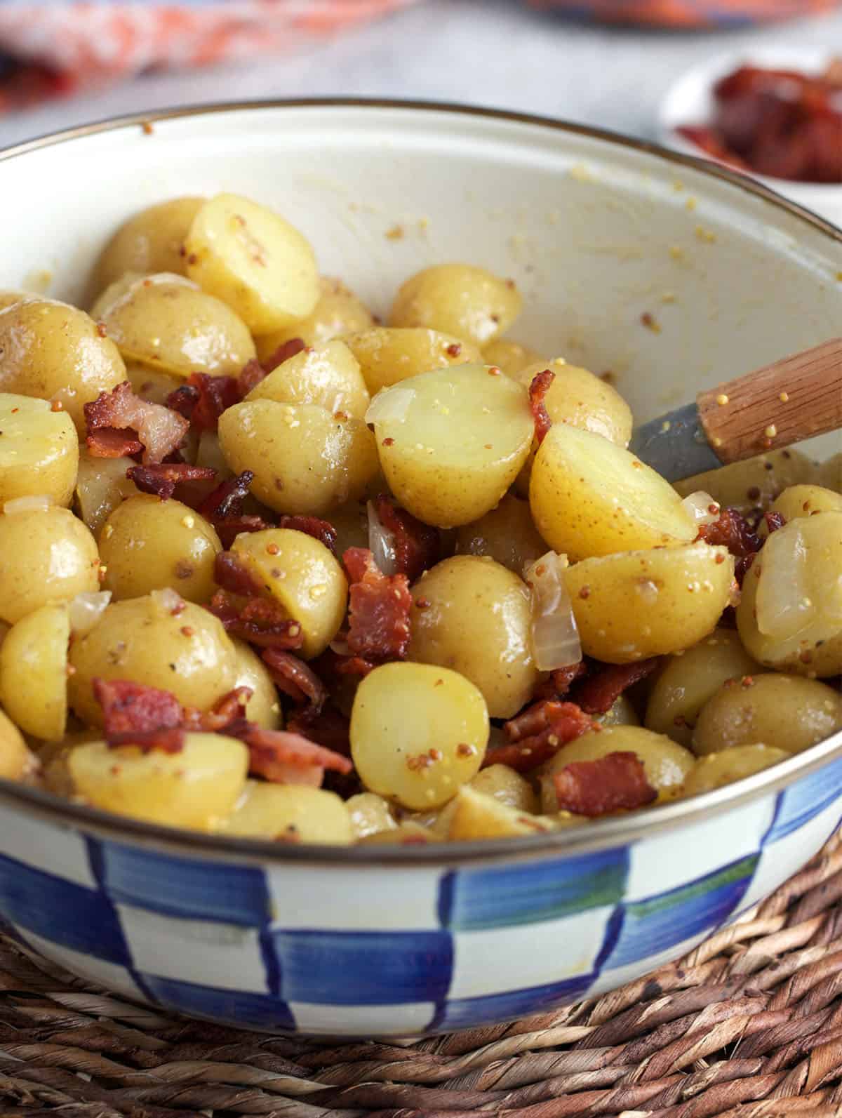 German potato salad being stirred together in a blue and white Mackenzie Childs bowl