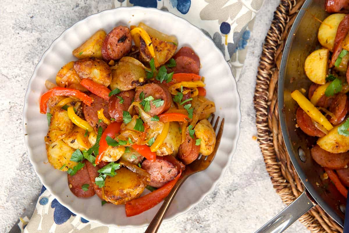 Smoked sausage and potatoes with red pepper and onions in a white bowl with a fork