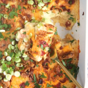 Mashed Potato Casserole in a white baking dish with a gold serving spoon
