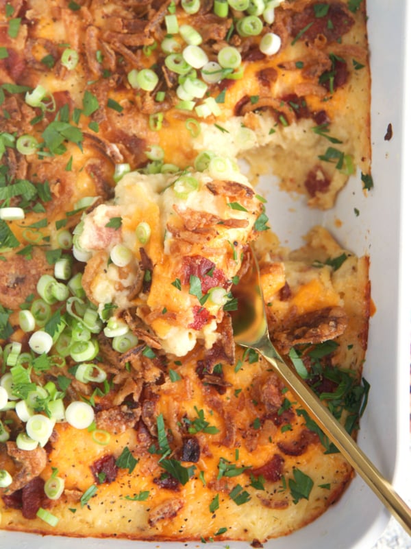 Mashed Potato Casserole in a white baking dish with a gold serving spoon