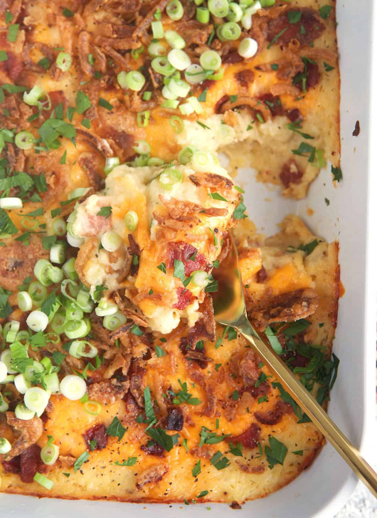 Mashed Potato Casserole in a white baking dish with a gold serving spoon