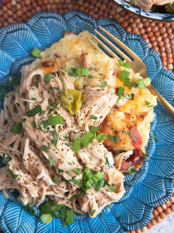 Mississippi chicken on a pile of mashed potatoes plated on a blue plate