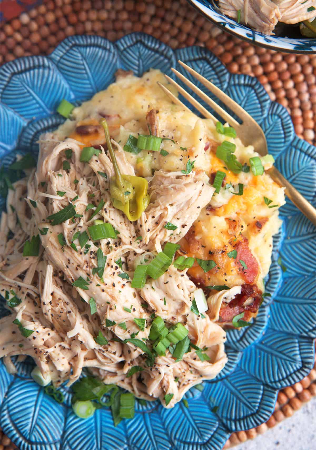 Mississippi chicken on a pile of mashed potatoes plated on a blue plate