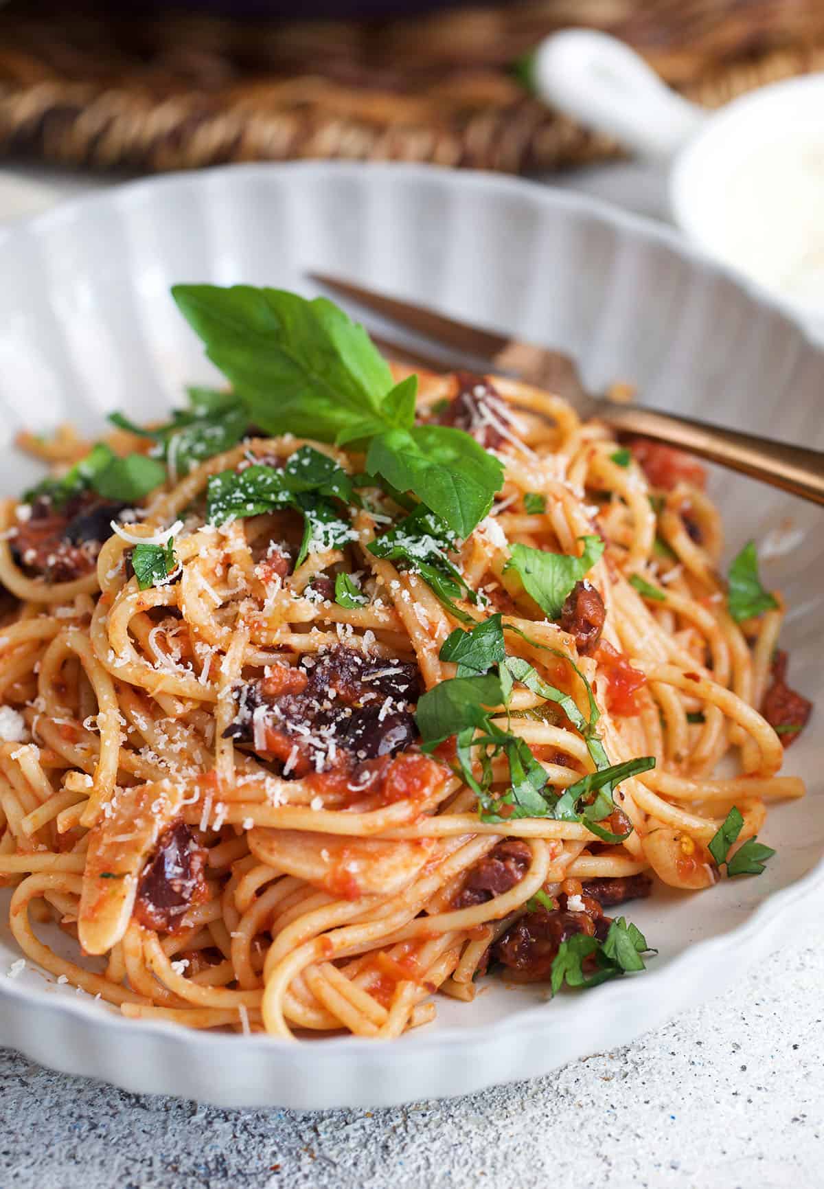 Pasta Puttanesca in a white bowl with basil on top