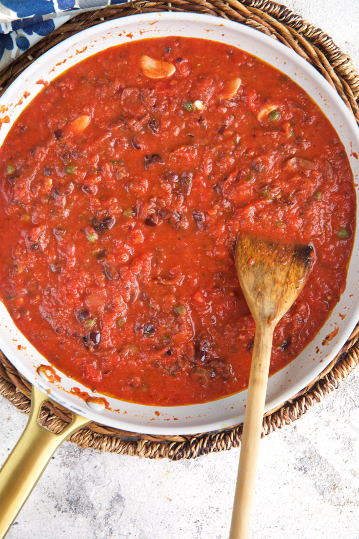 puttanesca sauce being stirred in a skillet with a wooden spoon