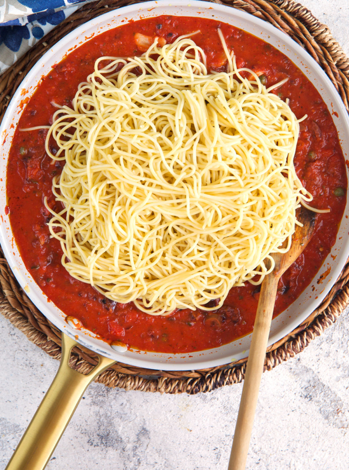 spaghetti in a pan of puttanesca sauce.