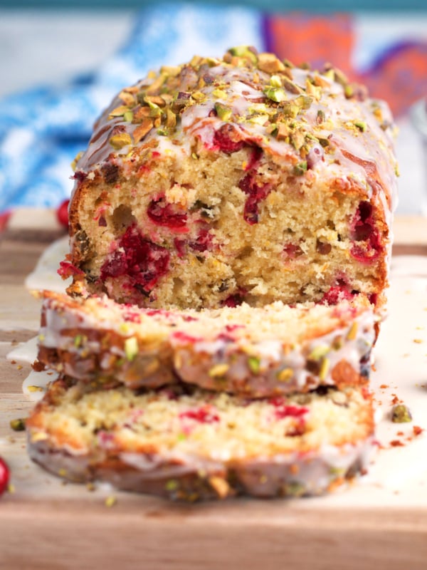 Pistachio Cranberry Bread with orange glaze on a cutting board with two slices