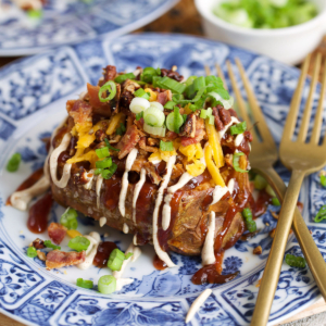 Pulled pork stuffed sweet potatoes on a blue and white plate topped with cheese and bacon.
