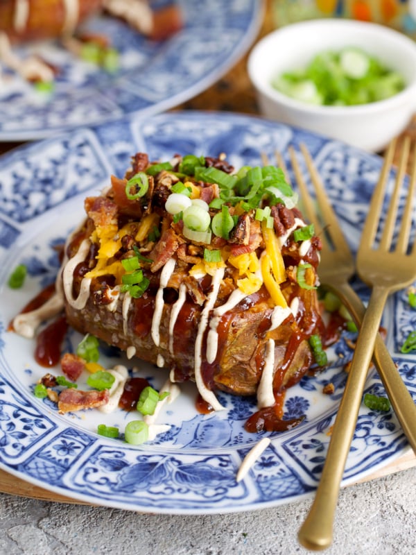 Pulled pork stuffed sweet potatoes on a blue and white plate topped with cheese and bacon.