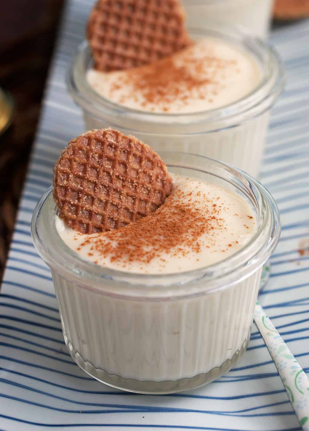 Vanilla pudding in glass cups with cinnamon on top and a mini stroopwafle