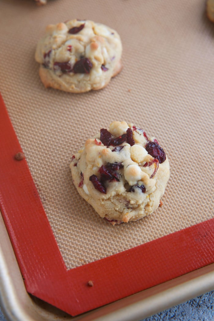 white chocolate cranberry cookies on a baking sheet with a silat mat