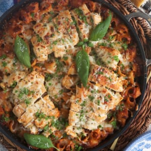 chicken parmesan pasta in a black skillet topped with fresh basil leaves
