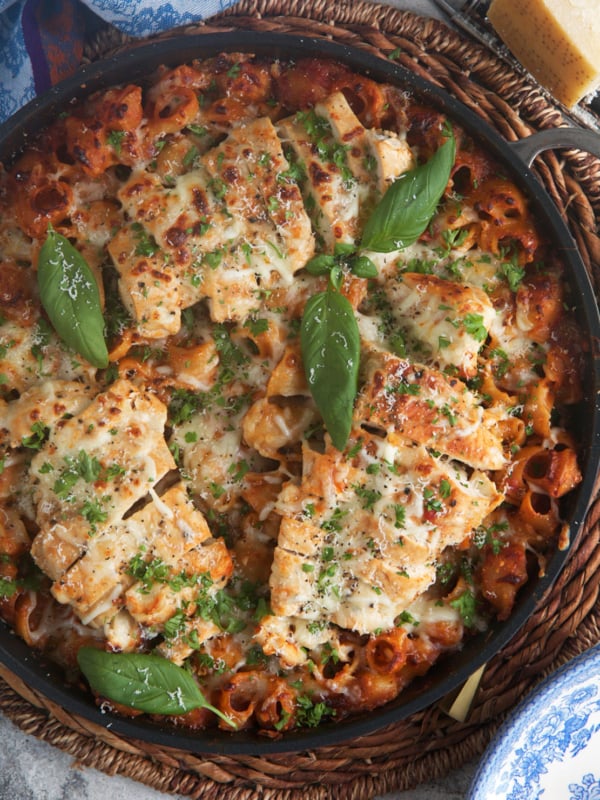 chicken parmesan pasta in a black skillet topped with fresh basil leaves