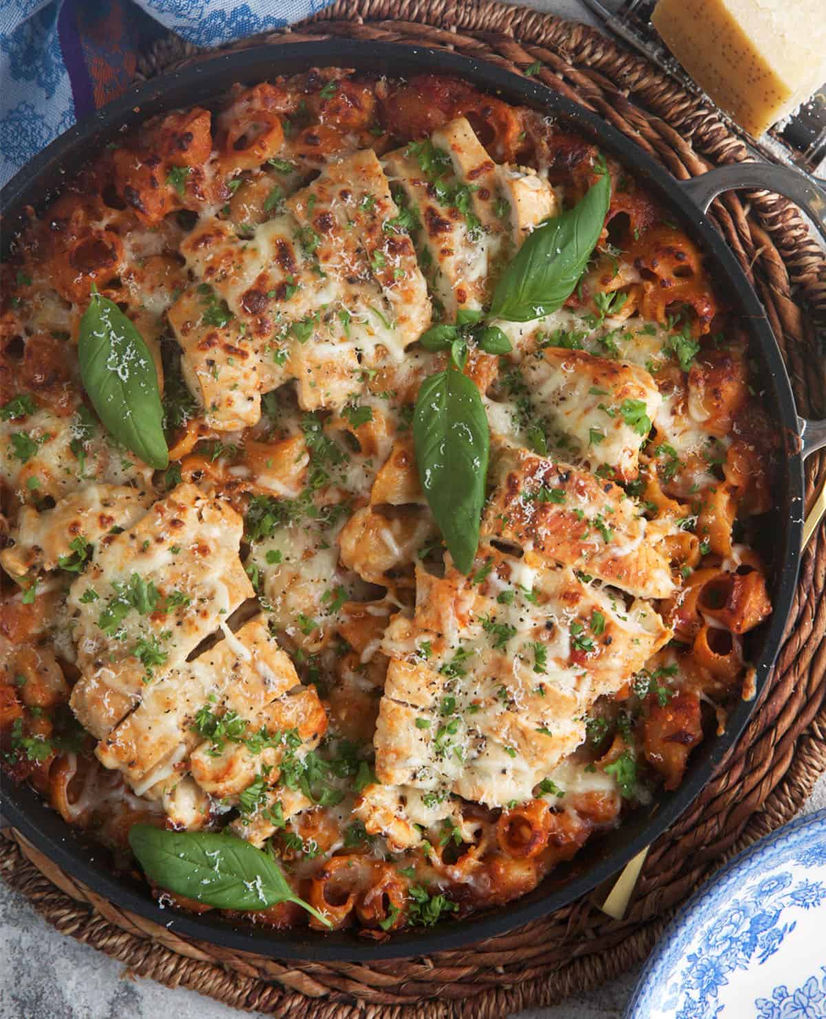 chicken parmesan pasta in a black skillet topped with fresh basil leaves