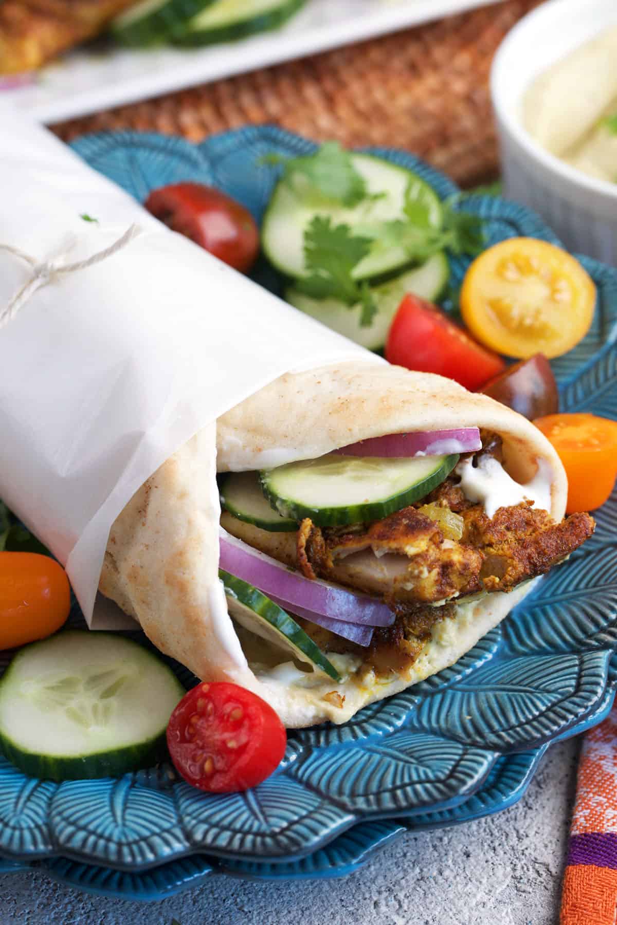 chicken shawarma wrap on a blue plate with cucumbers and tomatoes.
