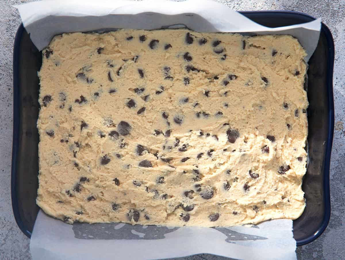 Chocolate Chip Cookie bar cookie dough in a baking dish with parchment.