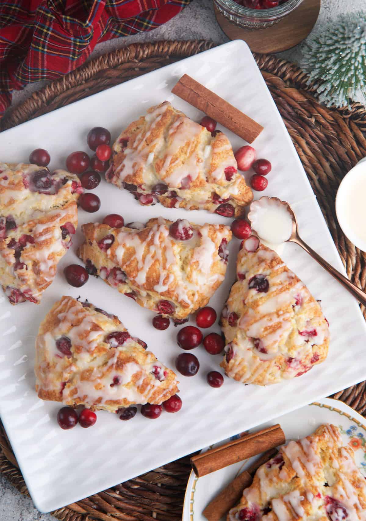 Cranberry Orange Scones on a square platter with cinnamon sticks and a spoon with glaze.