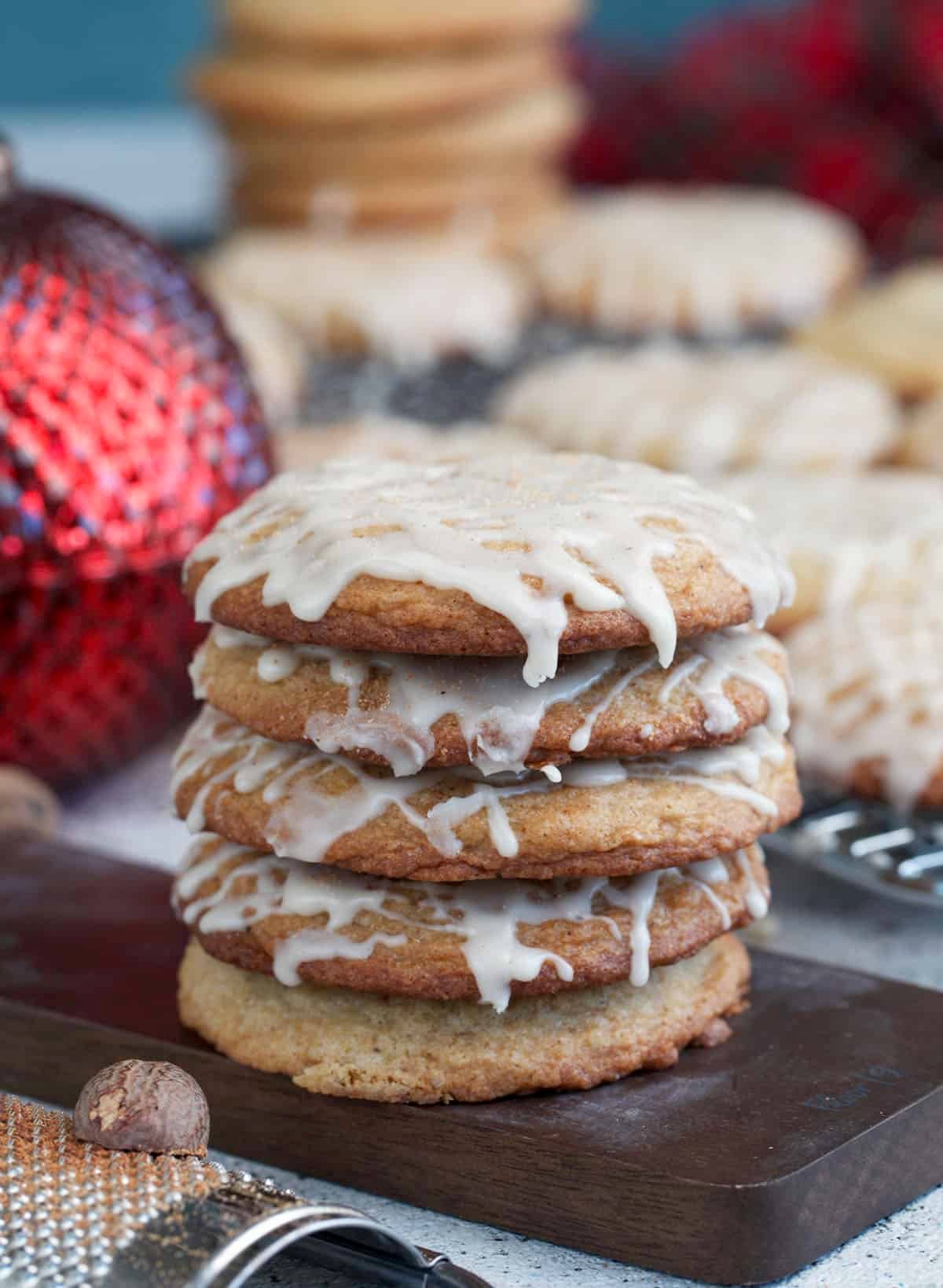 Eggnog cookies stacked on a small serving board with an ornament in the background.