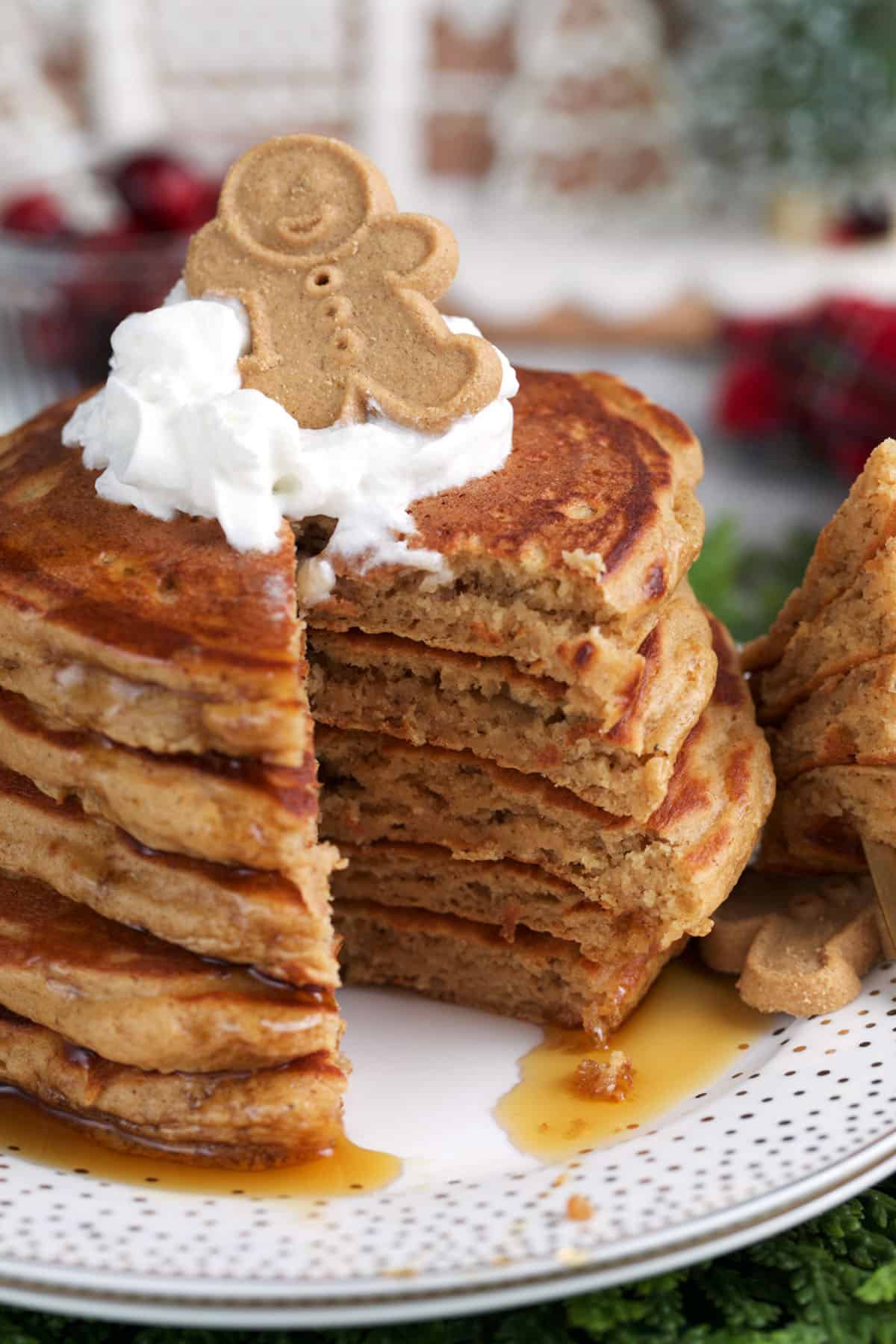 Gingerbread pancake stack with a wedge cut out and topped with whipped cream.