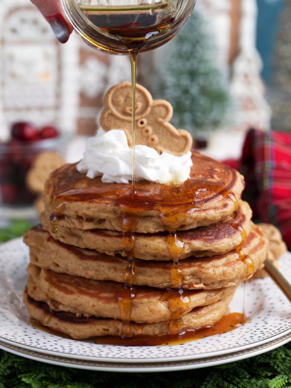 Gingerbread pancake stacked on a plate with whipped cream and a gingerbread man on top